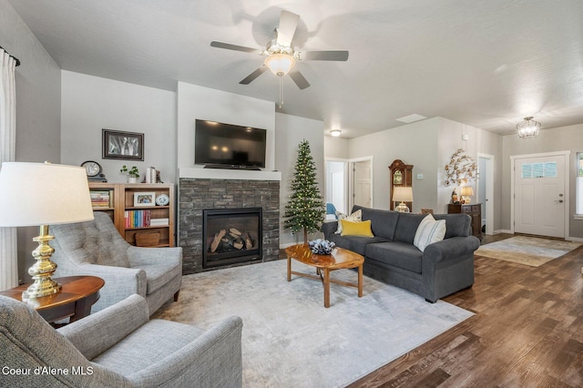 living room with a stone fireplace, wood-type flooring, and ceiling fan