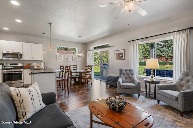 living room featuring a wealth of natural light, sink, dark wood-type flooring, and ceiling fan with notable chandelier