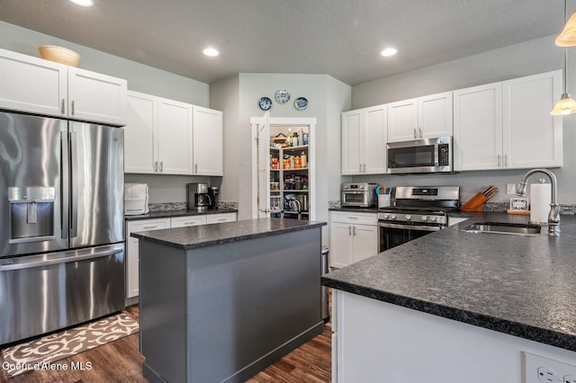 kitchen with white cabinetry, stainless steel appliances, sink, and hanging light fixtures