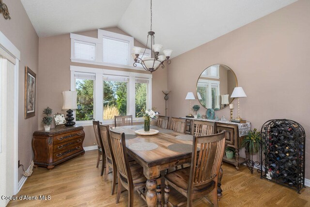 dining room with light wood-type flooring, a notable chandelier, and vaulted ceiling