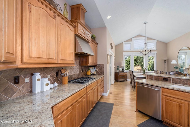 kitchen with appliances with stainless steel finishes, light stone countertops, an inviting chandelier, light wood-type flooring, and pendant lighting