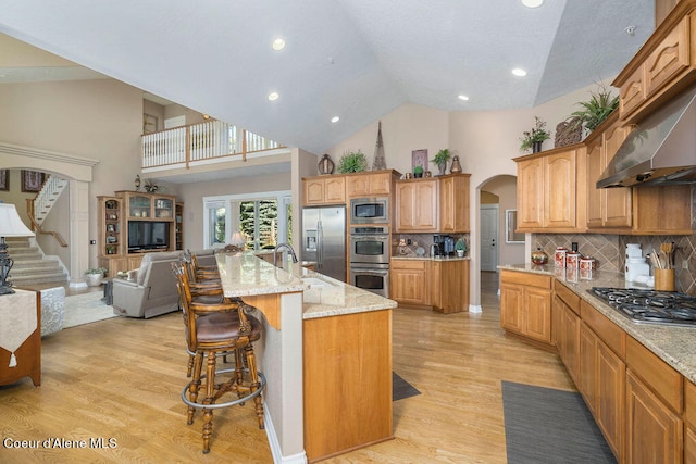 kitchen featuring stainless steel appliances, an island with sink, a kitchen breakfast bar, high vaulted ceiling, and light hardwood / wood-style flooring