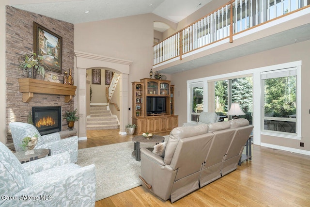 living room featuring light hardwood / wood-style floors, a stone fireplace, and high vaulted ceiling