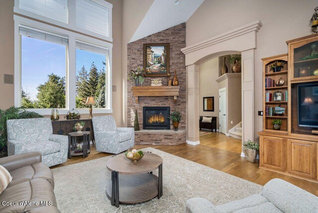 living room featuring high vaulted ceiling, a fireplace, and light hardwood / wood-style flooring