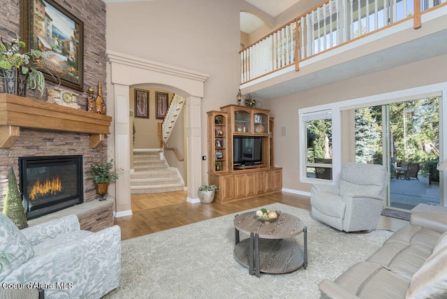 living room featuring a stone fireplace, wood-type flooring, and a high ceiling