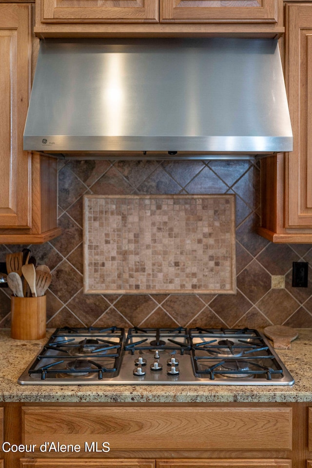 interior details featuring stainless steel gas cooktop, wall chimney exhaust hood, tasteful backsplash, and light stone countertops