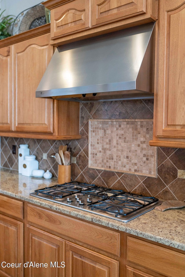 kitchen with light stone countertops, stainless steel gas cooktop, range hood, and decorative backsplash