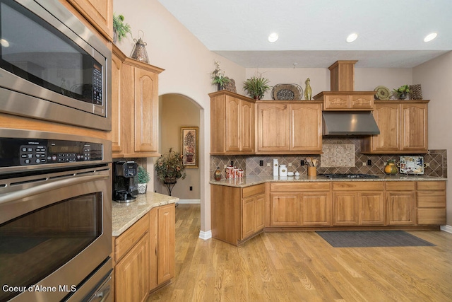 kitchen with appliances with stainless steel finishes, exhaust hood, light hardwood / wood-style floors, and backsplash