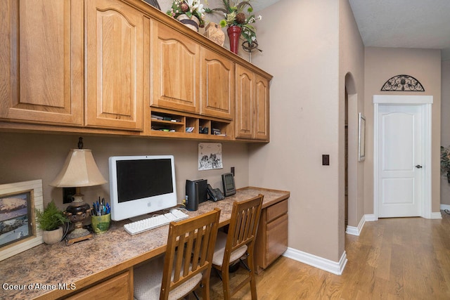 home office with light wood-type flooring, lofted ceiling, and built in desk