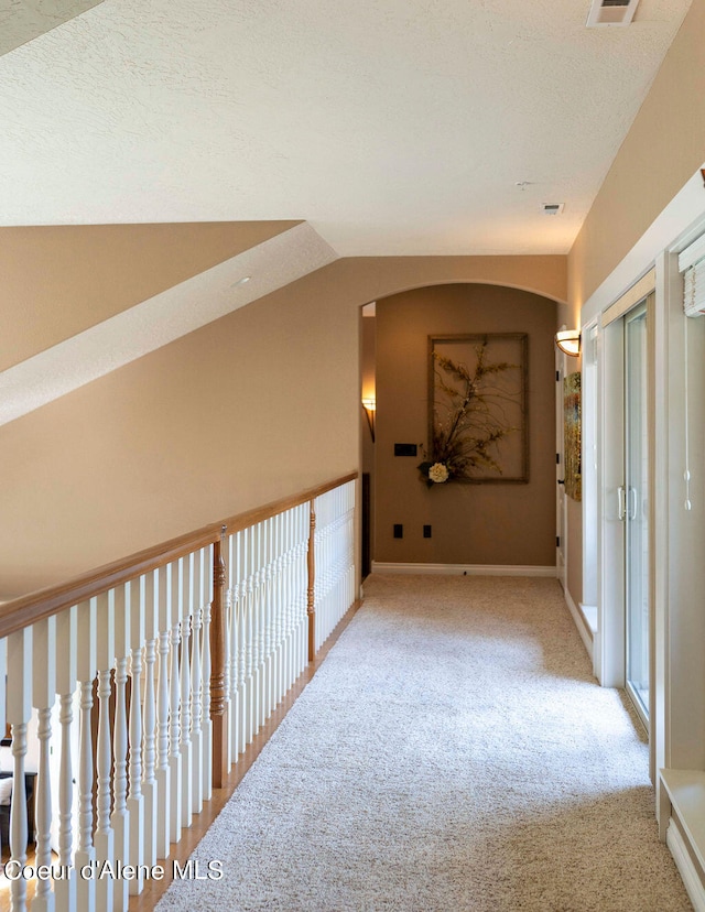 hall with carpet, vaulted ceiling, and a textured ceiling