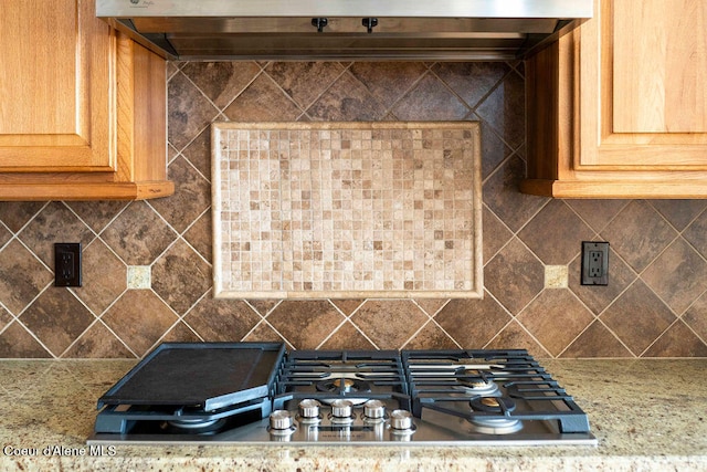 kitchen featuring light stone countertops, stainless steel gas cooktop, extractor fan, and tasteful backsplash