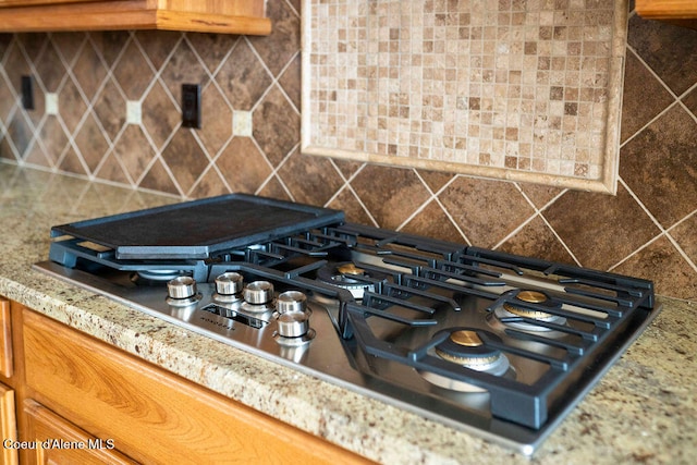 room details featuring light stone countertops, stainless steel gas stovetop, and backsplash