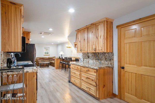 kitchen featuring sink, light stone countertops, light hardwood / wood-style flooring, and decorative backsplash