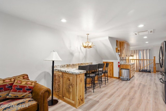 bar featuring light stone counters, stainless steel fridge, decorative light fixtures, and light wood-type flooring