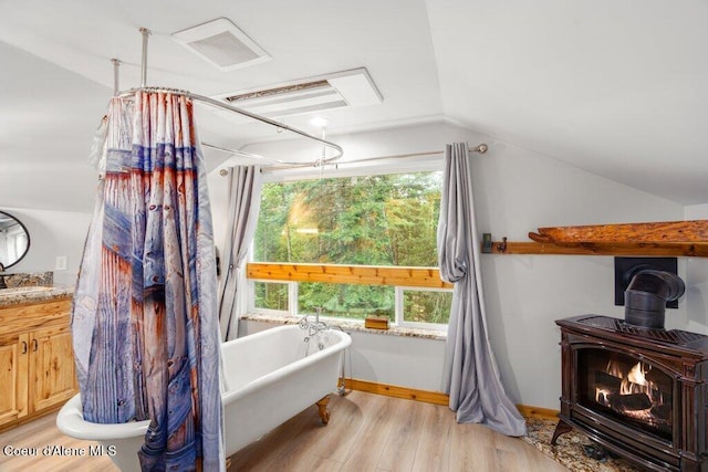 bathroom with lofted ceiling, hardwood / wood-style floors, a healthy amount of sunlight, a bath, and a wood stove