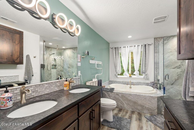 full bathroom featuring plus walk in shower, hardwood / wood-style flooring, toilet, vanity, and a textured ceiling