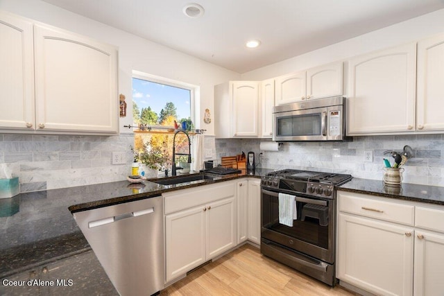 kitchen with sink, white cabinetry, stainless steel appliances, and dark stone counters