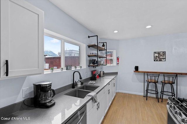 kitchen with sink, white cabinetry, stainless steel appliances, light stone counters, and light hardwood / wood-style flooring