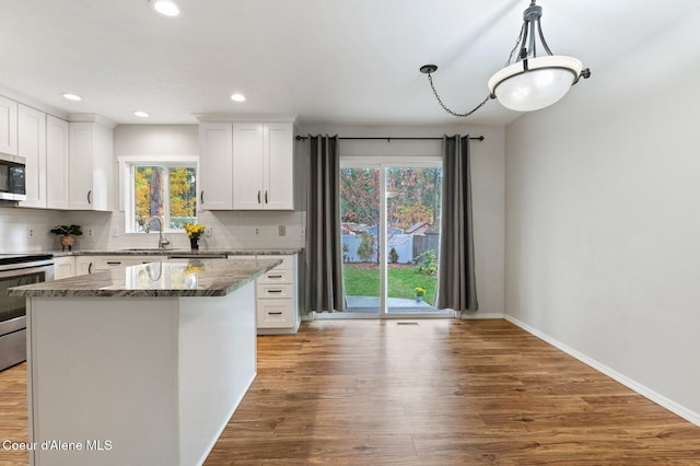 kitchen featuring white cabinets, backsplash, pendant lighting, light hardwood / wood-style floors, and stainless steel appliances