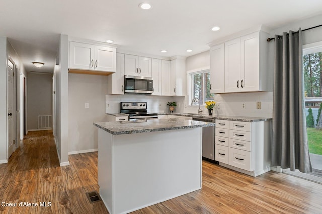 kitchen featuring a wealth of natural light, a kitchen island, appliances with stainless steel finishes, and white cabinetry