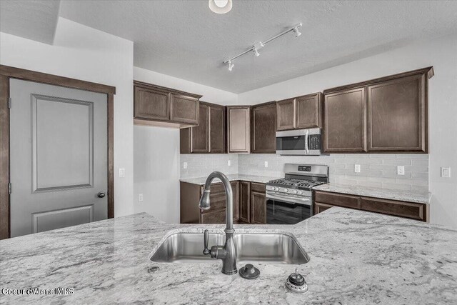 2711 E Cinder Ave, Post Falls, ID 83854 - kitchen with stainless steel appliances, a sink, light stone counters, decorative backsplash, and dark brown cabinets