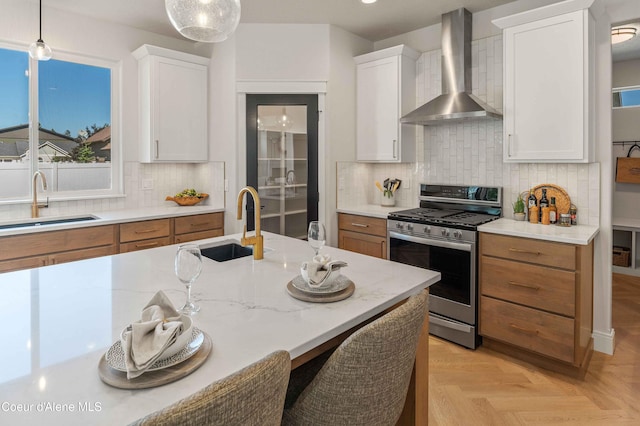 kitchen with wall chimney range hood, white cabinets, hanging light fixtures, and stainless steel gas stove