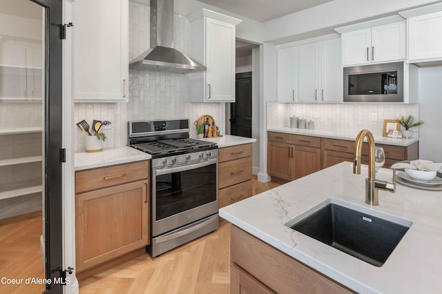 kitchen with light stone counters, white cabinetry, sink, wall chimney exhaust hood, and stainless steel appliances