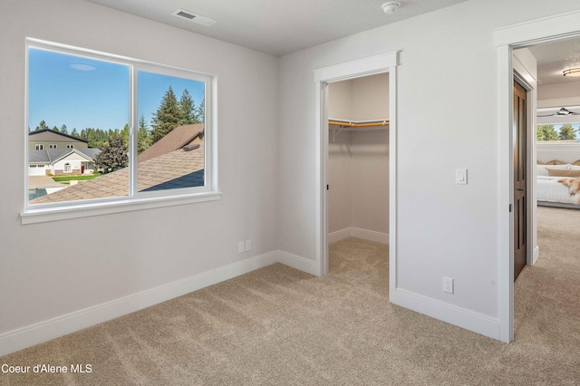 unfurnished bedroom featuring light carpet, a walk in closet, and a closet