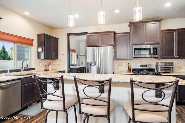 kitchen with sink, a kitchen bar, dark hardwood / wood-style flooring, hanging light fixtures, and stainless steel appliances