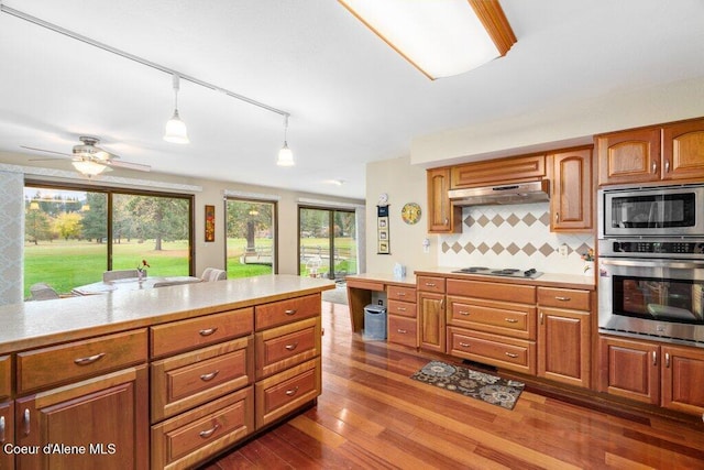 kitchen with exhaust hood, brown cabinets, light countertops, stainless steel appliances, and tasteful backsplash