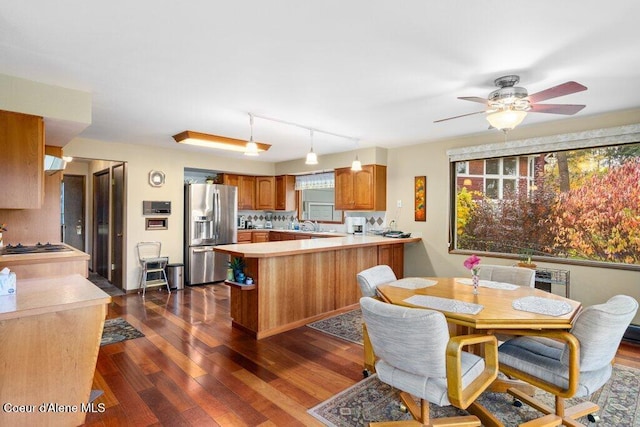 kitchen with ceiling fan, brown cabinetry, dark wood-style flooring, stainless steel refrigerator with ice dispenser, and a peninsula