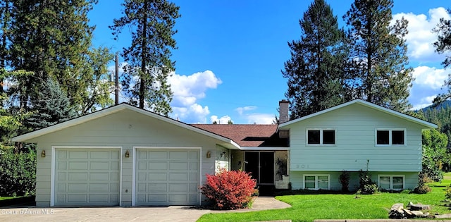 split level home with an attached garage, driveway, a chimney, and a front lawn