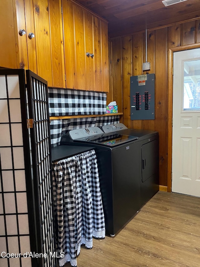 clothes washing area featuring light hardwood / wood-style floors, washer and clothes dryer, wooden walls, wooden ceiling, and electric panel