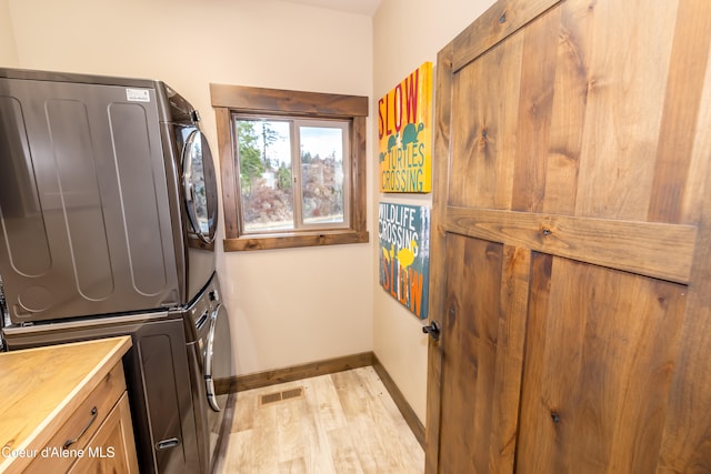 washroom featuring light hardwood / wood-style flooring, cabinets, and stacked washer / drying machine