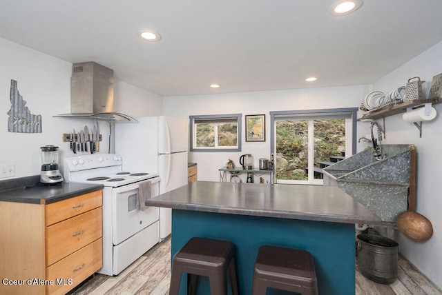 kitchen featuring white appliances, a kitchen bar, wall chimney exhaust hood, light hardwood / wood-style flooring, and light brown cabinets