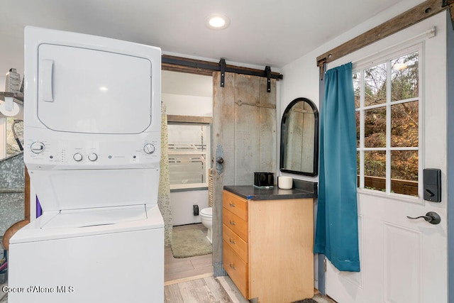 clothes washing area featuring light hardwood / wood-style floors, stacked washing maching and dryer, and a barn door