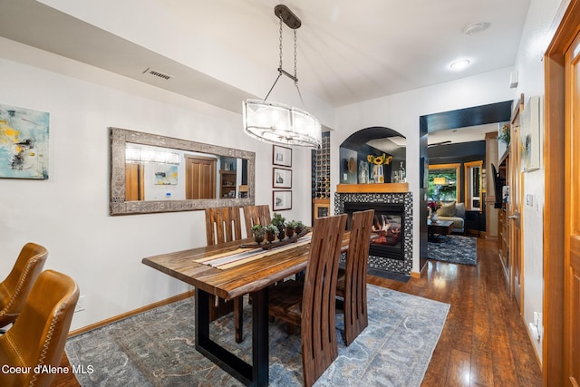 dining space featuring dark hardwood / wood-style floors, a tile fireplace, and an inviting chandelier