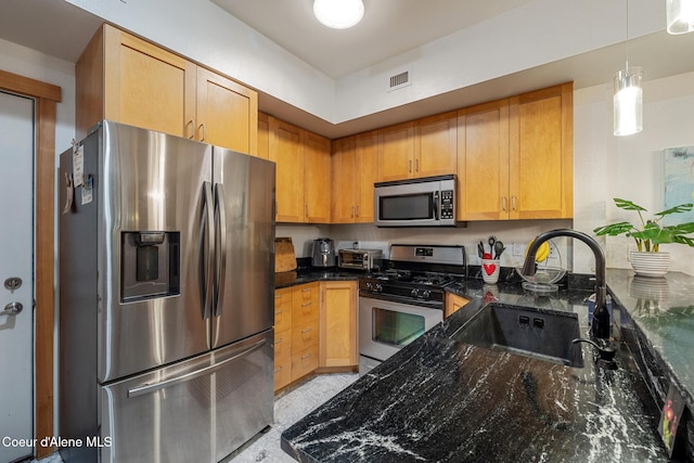 kitchen with hanging light fixtures, appliances with stainless steel finishes, dark stone counters, and sink