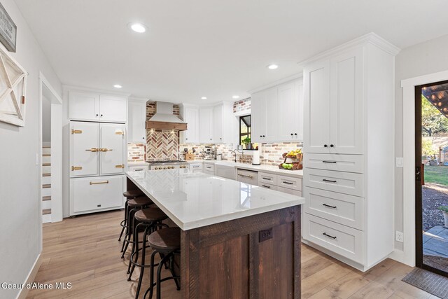 kitchen with built in fridge, a center island, white cabinets, premium range hood, and light hardwood / wood-style floors