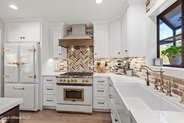 kitchen featuring white cabinets, high end stainless steel range oven, custom range hood, white fridge, and sink