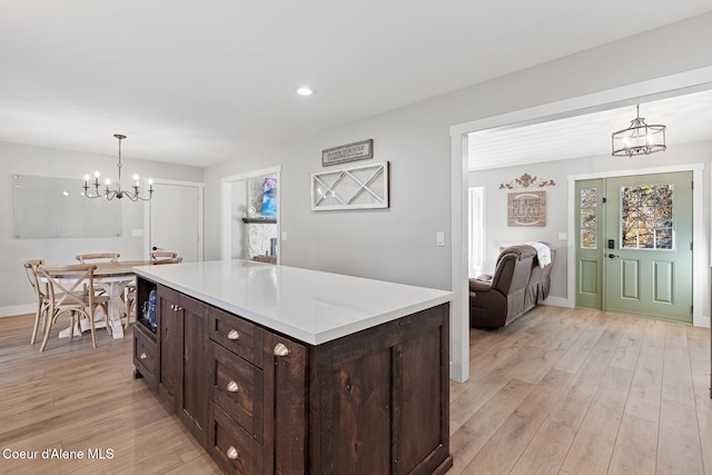 kitchen with a kitchen island, dark brown cabinetry, pendant lighting, light hardwood / wood-style flooring, and a chandelier