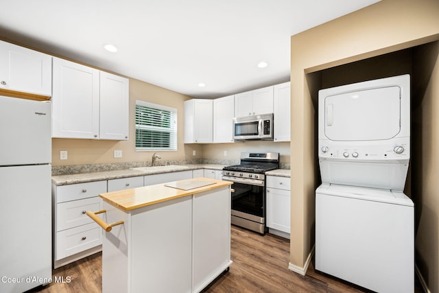 kitchen with white cabinets, stainless steel appliances, stacked washer / dryer, and sink