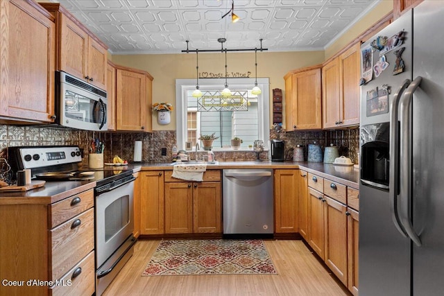 kitchen featuring appliances with stainless steel finishes, an ornate ceiling, light wood-style floors, decorative backsplash, and crown molding