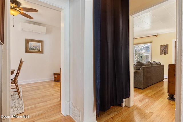hallway with an AC wall unit, light wood-type flooring, baseboards, and ornamental molding