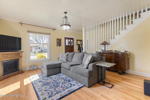 living area with wood finished floors, baseboards, a fireplace, ornamental molding, and stairway