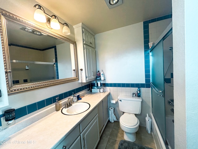 full bathroom featuring toilet, tile patterned flooring, vanity, bath / shower combo with glass door, and tile walls