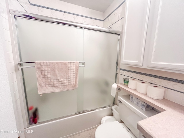 bathroom featuring enclosed tub / shower combo, toilet, and tile patterned flooring