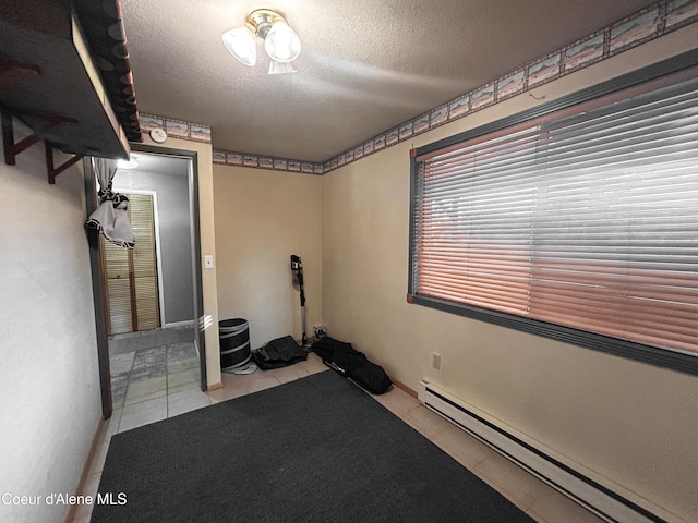 exercise room featuring a textured ceiling, baseboard heating, and light tile patterned flooring