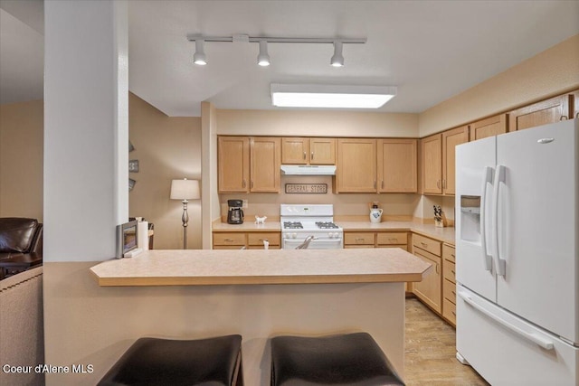 kitchen with light brown cabinetry, a kitchen breakfast bar, kitchen peninsula, and white appliances