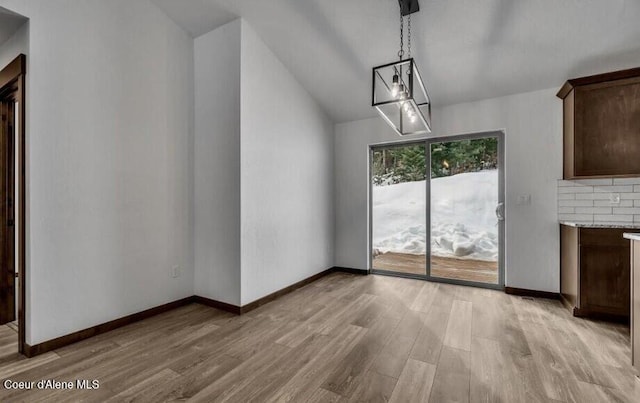 unfurnished dining area featuring light wood-type flooring, vaulted ceiling, and a notable chandelier